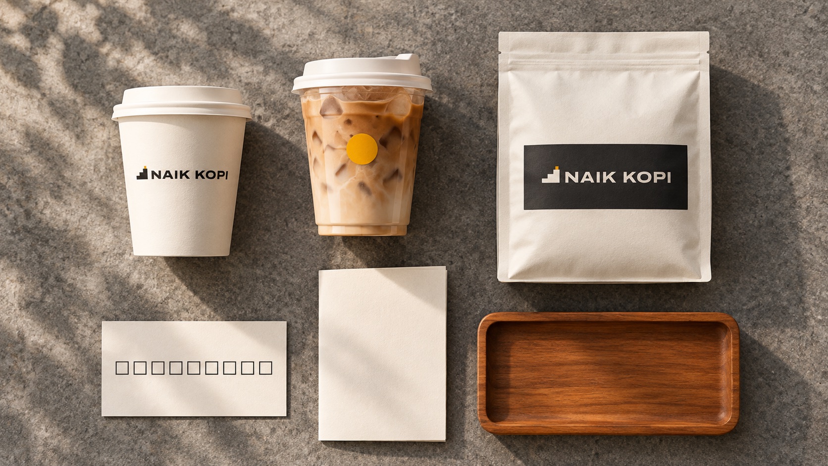 Flatlay kemasan Naik Kopi di atas batu andesit: cup panas, cup es, kantong biji, kartu stempel, kartu menu, nampan jati